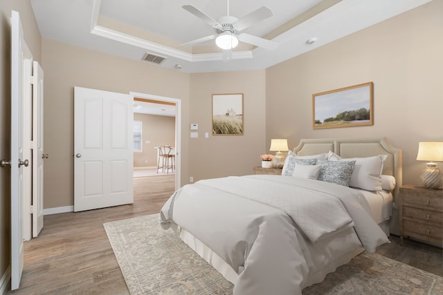 bedroom with a tray ceiling, ceiling fan, and light hardwood / wood-style floors