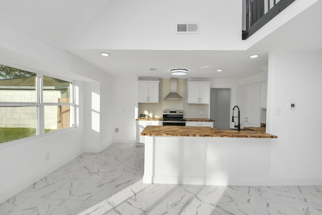 kitchen featuring kitchen peninsula, stainless steel electric stove, wall chimney range hood, white cabinets, and butcher block counters