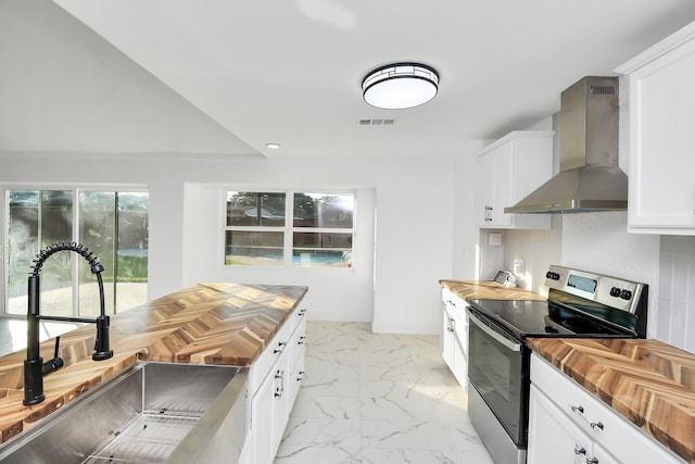 kitchen with wooden counters, sink, wall chimney exhaust hood, stainless steel electric range oven, and white cabinetry