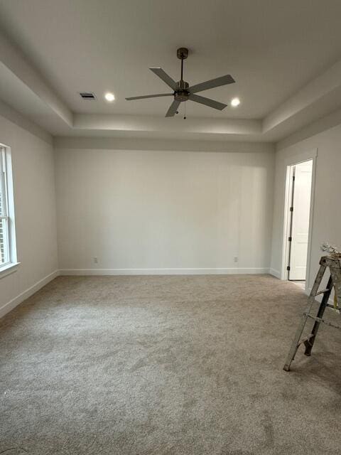 empty room featuring carpet flooring, a raised ceiling, and ceiling fan