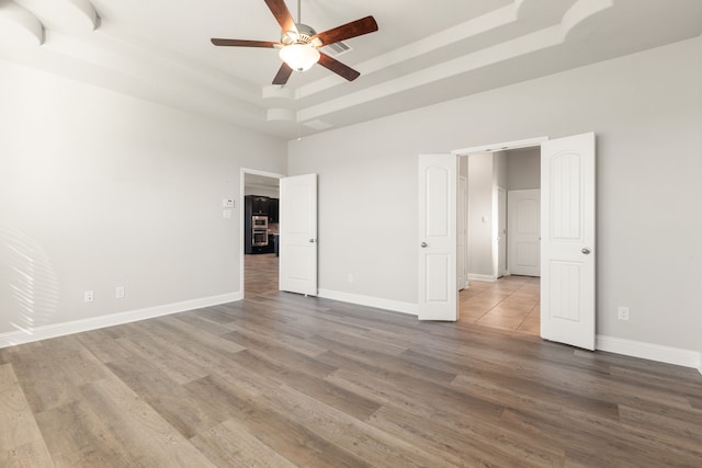 unfurnished bedroom featuring a raised ceiling, ceiling fan, and wood-type flooring