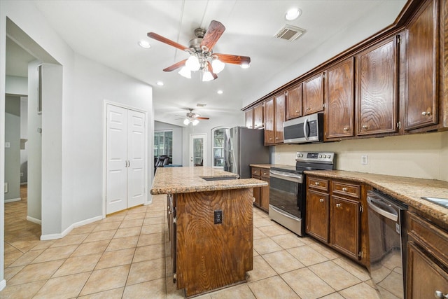 kitchen with ceiling fan, stainless steel appliances, a kitchen island, dark brown cabinets, and light tile patterned flooring