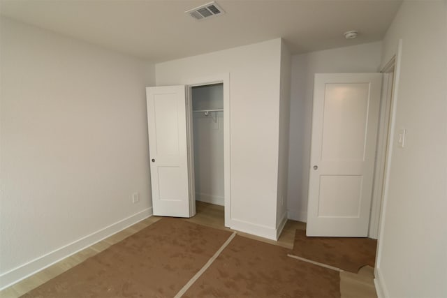 unfurnished bedroom featuring a closet, visible vents, baseboards, and wood finished floors