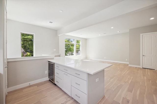 kitchen with kitchen peninsula, light wood-type flooring, white cabinetry, and beverage cooler