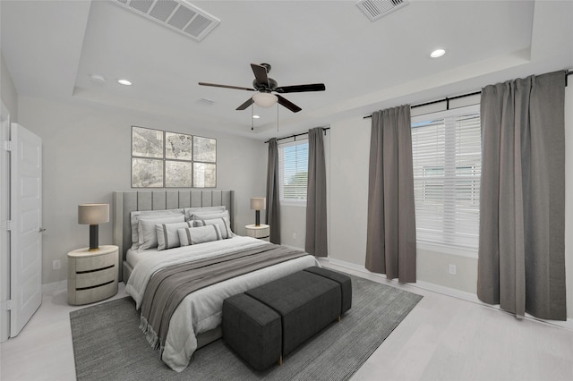 bedroom with a raised ceiling, ceiling fan, and light wood-type flooring