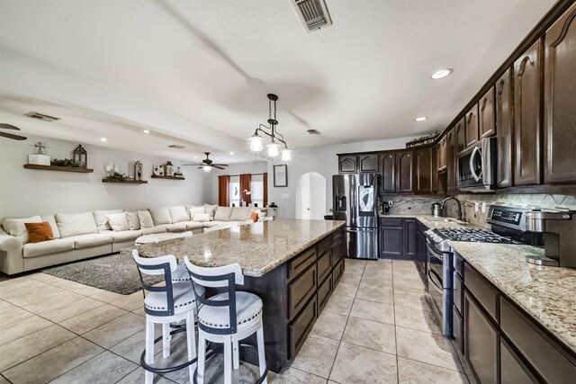 kitchen with appliances with stainless steel finishes, light stone counters, dark brown cabinetry, decorative light fixtures, and a kitchen island