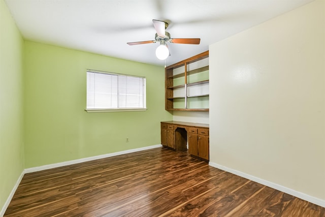 unfurnished office featuring ceiling fan, baseboards, dark wood-style flooring, and built in desk