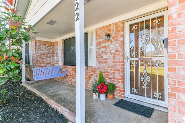 property entrance with covered porch, brick siding, and visible vents