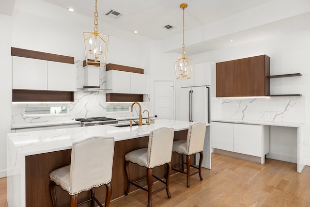 kitchen with an inviting chandelier, sink, pendant lighting, white cabinets, and an island with sink