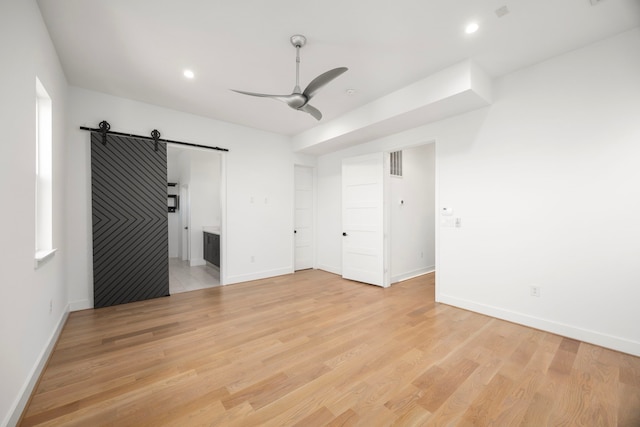 unfurnished bedroom featuring ensuite bathroom, light hardwood / wood-style floors, ceiling fan, and a barn door