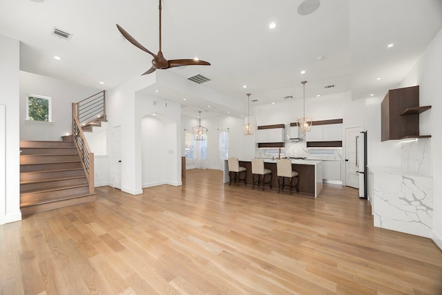 unfurnished living room with ceiling fan with notable chandelier and light hardwood / wood-style floors