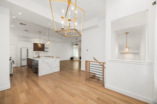 kitchen featuring a center island with sink, light stone countertops, light hardwood / wood-style floors, pendant lighting, and sink