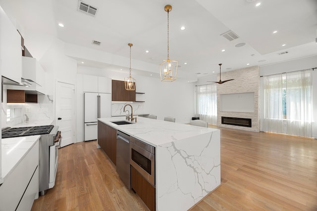 kitchen featuring white cabinetry, an island with sink, decorative light fixtures, built in appliances, and sink