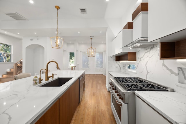 kitchen with stainless steel appliances, light stone counters, white cabinets, decorative light fixtures, and sink