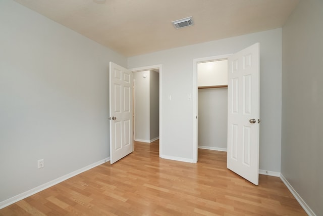 unfurnished bedroom with a closet, a walk in closet, and light hardwood / wood-style floors