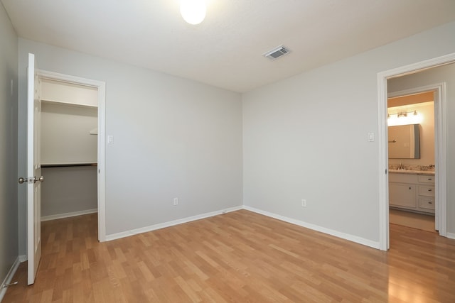 unfurnished bedroom with light wood-type flooring, a walk in closet, a closet, and sink