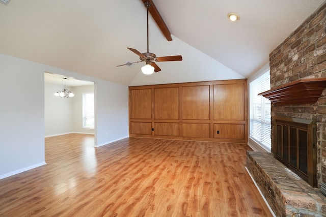 unfurnished living room featuring a brick fireplace, light hardwood / wood-style flooring, vaulted ceiling with beams, and ceiling fan with notable chandelier