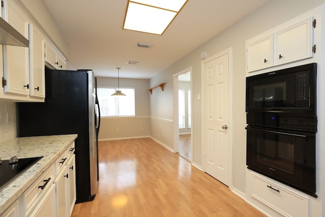 kitchen featuring black appliances, decorative light fixtures, wall chimney exhaust hood, and white cabinetry