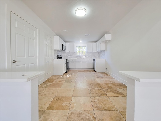 kitchen with appliances with stainless steel finishes, backsplash, sink, white cabinetry, and light tile patterned flooring