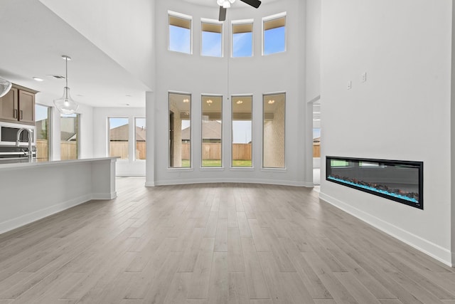 unfurnished living room with ceiling fan, light hardwood / wood-style flooring, a towering ceiling, and sink