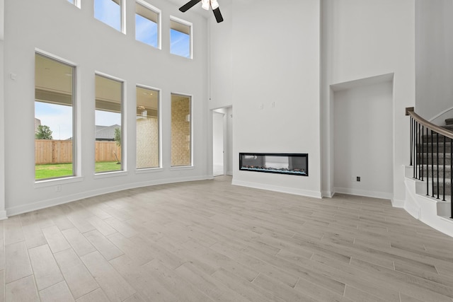 unfurnished living room featuring ceiling fan, light hardwood / wood-style flooring, and a towering ceiling