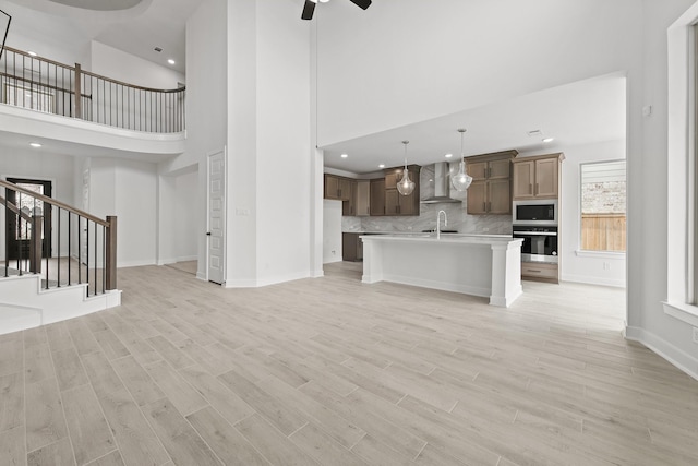 unfurnished living room with ceiling fan, sink, a towering ceiling, and light wood-type flooring