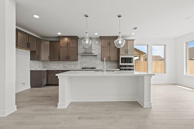 kitchen with pendant lighting, white microwave, a kitchen island with sink, and wall chimney exhaust hood