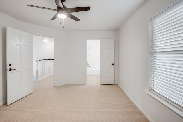 unfurnished bedroom featuring ceiling fan, light colored carpet, connected bathroom, and multiple windows