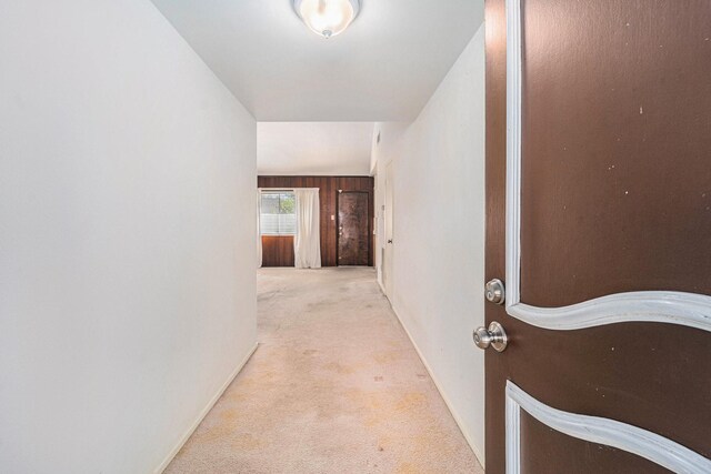 hallway with light carpet, vaulted ceiling, and wood walls