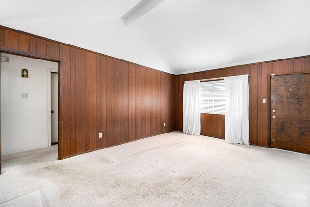 spare room with wooden walls, beamed ceiling, light colored carpet, and high vaulted ceiling