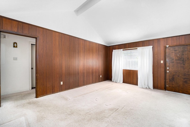 spare room featuring wooden walls, light colored carpet, and vaulted ceiling with beams