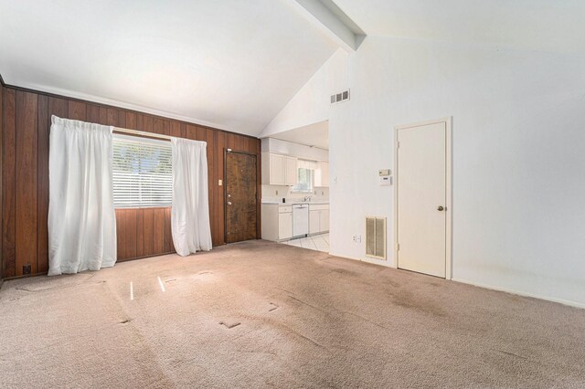 unfurnished living room featuring wood walls, beam ceiling, light colored carpet, and high vaulted ceiling