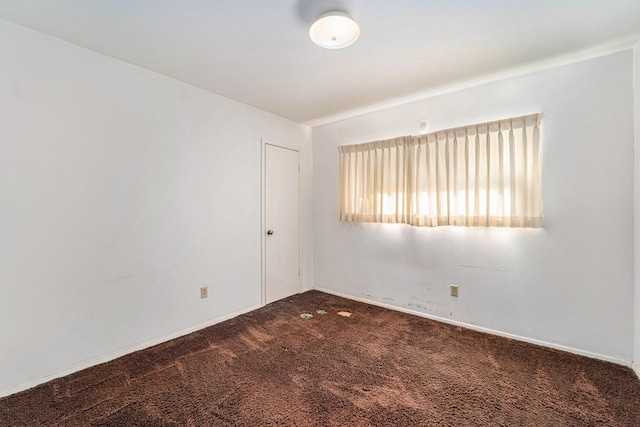 empty room with dark colored carpet and baseboards