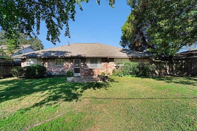 rear view of house featuring brick siding, a lawn, a shingled roof, and a fenced backyard