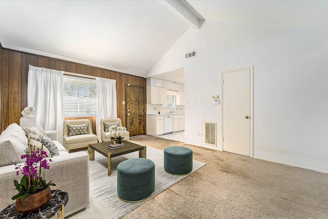 living area with beamed ceiling, wooden walls, light colored carpet, and visible vents