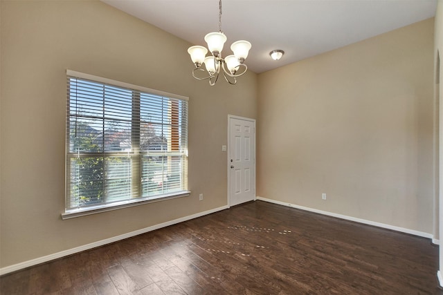 spare room featuring a chandelier, a healthy amount of sunlight, and dark hardwood / wood-style floors