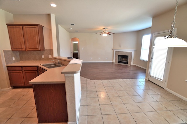 kitchen with a tile fireplace, ceiling fan, sink, light hardwood / wood-style flooring, and kitchen peninsula