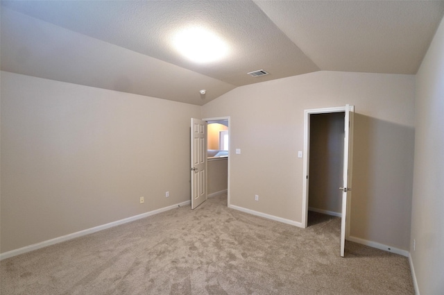 unfurnished bedroom with a textured ceiling, light colored carpet, and lofted ceiling