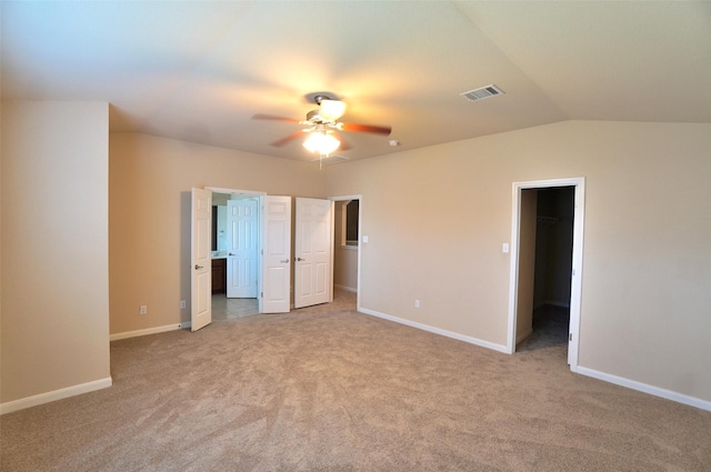 unfurnished bedroom featuring vaulted ceiling, light colored carpet, a spacious closet, and ceiling fan