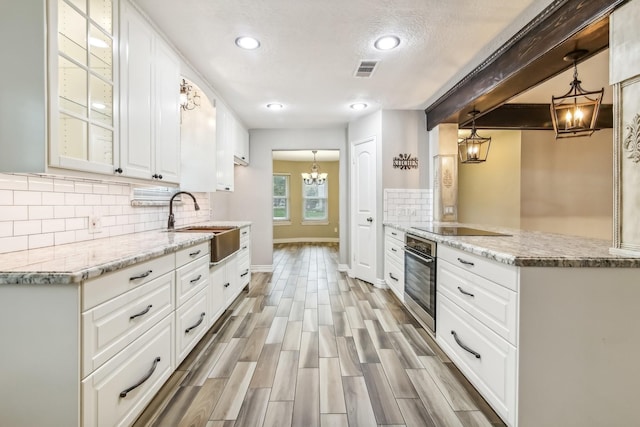 kitchen with kitchen peninsula, light wood-type flooring, pendant lighting, white cabinets, and oven