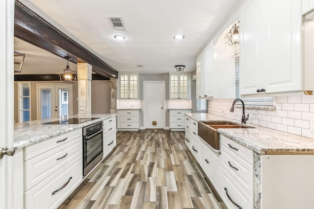 kitchen featuring oven, sink, black electric cooktop, light hardwood / wood-style floors, and white cabinetry