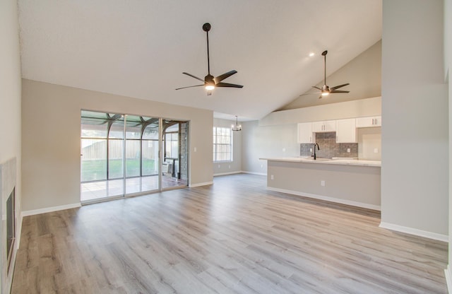 unfurnished living room featuring plenty of natural light, light hardwood / wood-style floors, sink, and high vaulted ceiling