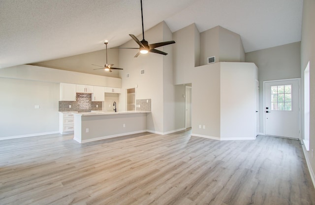 unfurnished living room with sink, a textured ceiling, high vaulted ceiling, and light hardwood / wood-style flooring