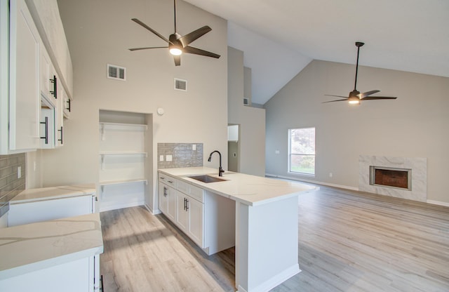 kitchen with kitchen peninsula, light stone counters, sink, high vaulted ceiling, and white cabinetry