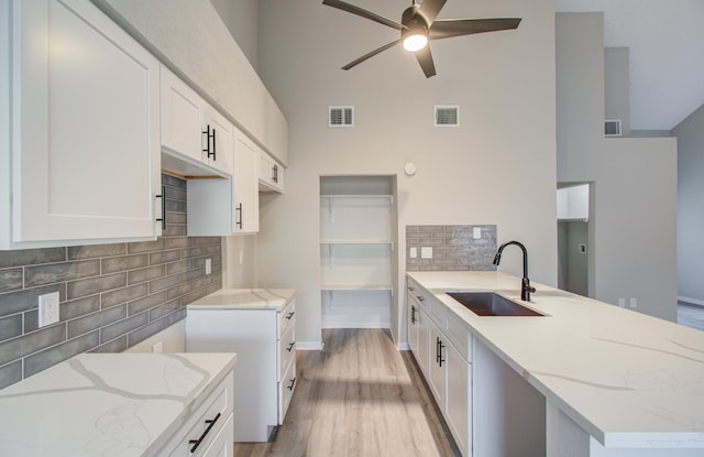 kitchen featuring light stone countertops, backsplash, sink, light hardwood / wood-style floors, and white cabinetry