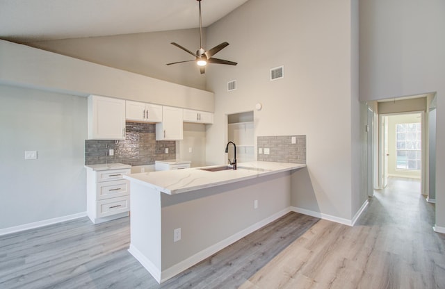 kitchen with backsplash, high vaulted ceiling, white cabinets, sink, and kitchen peninsula