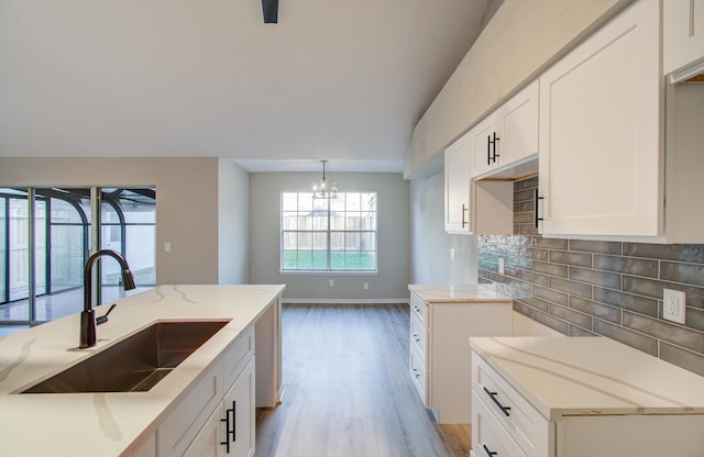 kitchen with a kitchen island with sink, white cabinets, sink, light hardwood / wood-style floors, and a chandelier