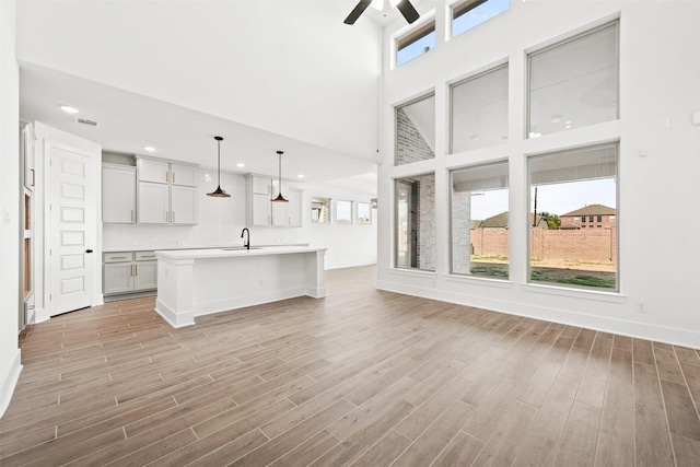 kitchen with sink, light hardwood / wood-style flooring, a towering ceiling, an island with sink, and decorative light fixtures