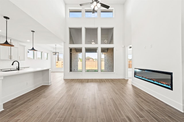 unfurnished living room featuring ceiling fan, sink, a towering ceiling, and wood-type flooring