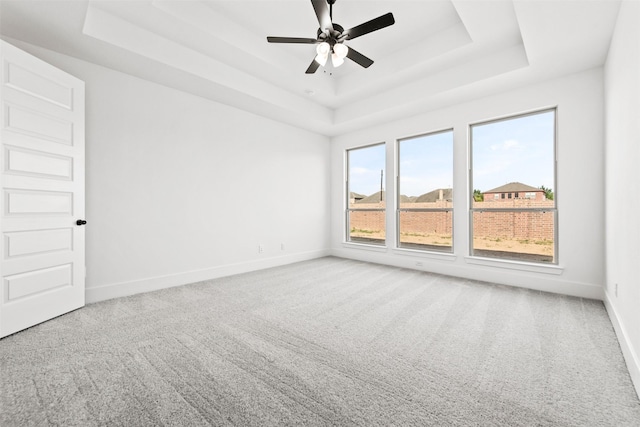 empty room featuring a raised ceiling, ceiling fan, and light colored carpet